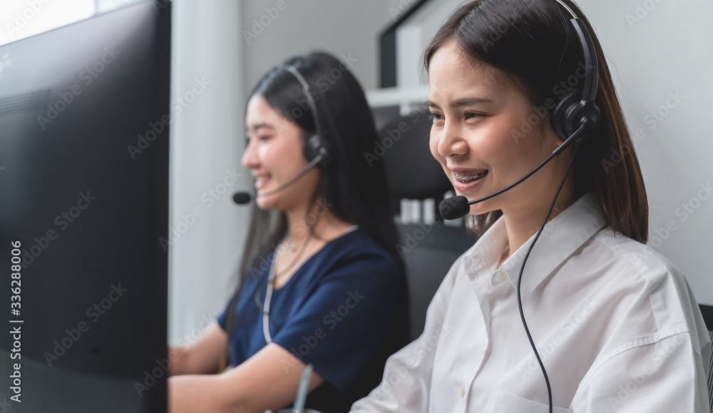 Smiling Asian business woman and team working in call center at office desk with headset and computer.