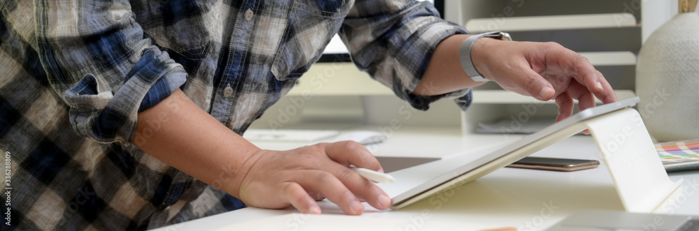 Cropped shot of male designer standing and working on digital tablet in office room Cropped shot of male designer standing and working on digital tablet in office room