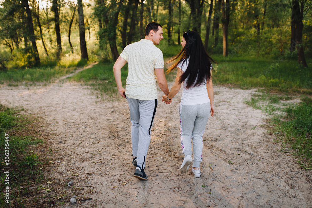 Fototapeta premium Loving guy and girl run through the forest, in nature, in tracksuits for a walk, holding hands. Love story newlyweds. Photography, concept.