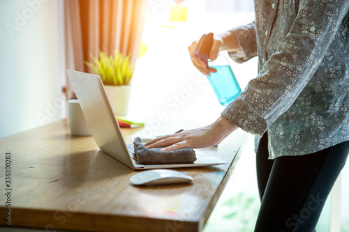 Bussiness worman work from home wearing protection mark in covid-19 virus situation. Her working in quarantine for coronavirus and clening her laptop with sanitizer/alcohol gel. photo