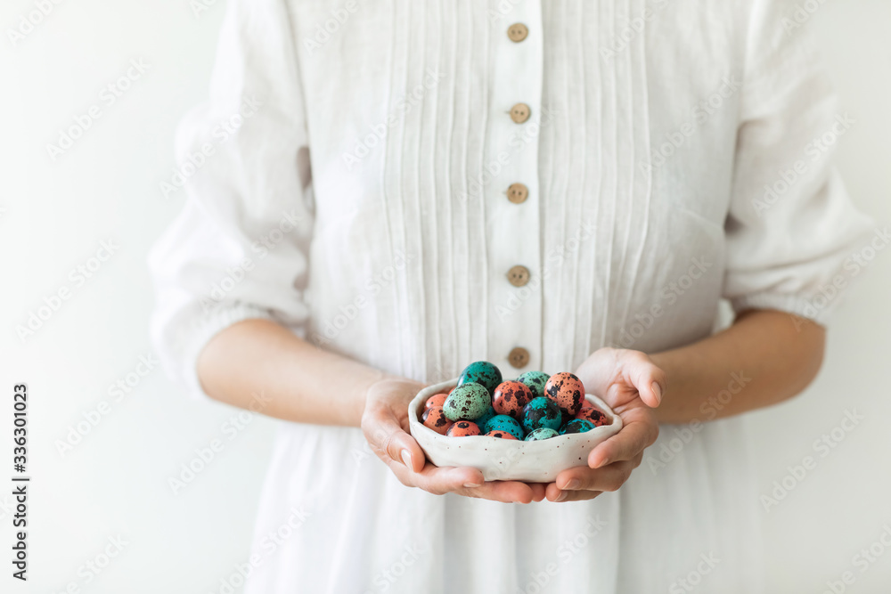 Woman hands holding small beautiful ceramic plate with painted quail eggs for Easter. White rustic dress, red and blue trendy color of eggs. Woman hands holding small beautiful ceramic plate with painted quail eggs for Easter. White rustic dress, red and blue trendy color of eggs.