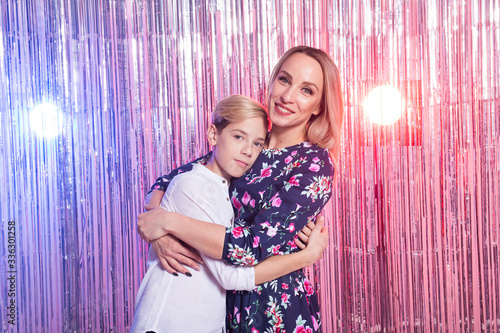Mothers day, children and family concept - teen boy and his mom embracing on shiny party background.
