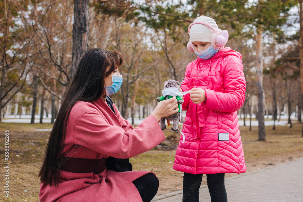 Mom and daughter walk in the park during quarantine of the coronavirus. Baby and parent in protective medical masks. A woman with a child wears a mask on a toy. Pandemic COVID-19 Mom and daughter walk in the park during quarantine of the coronavirus. Baby and parent in protective medical masks. A woman with a child wears a mask on a toy. Pandemic COVID-19