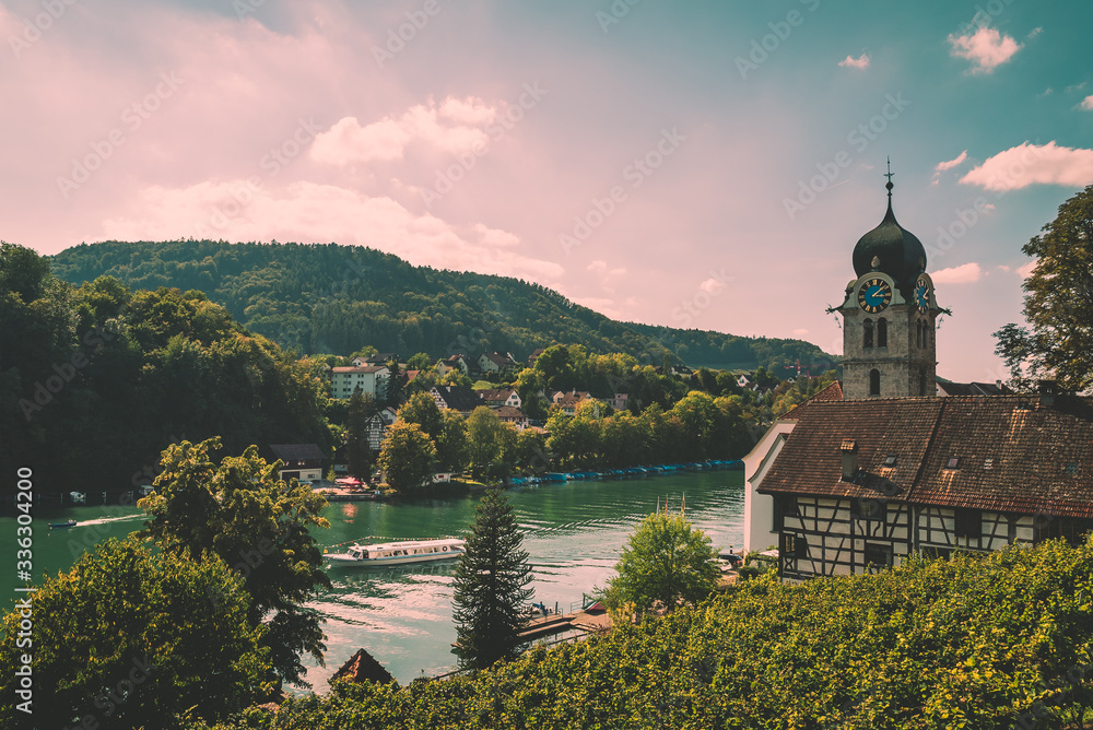 Scenic view of the river Rhine in the town of Eglisau Switzerland, overlooking a clock tower church with green trees and hills in the background
