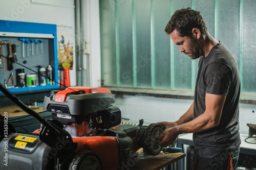 Obraz na płótnie Professional serviceman is repairing a lawnmower, refitting a front wheel. Man repairing a mower in a workshop w salonie