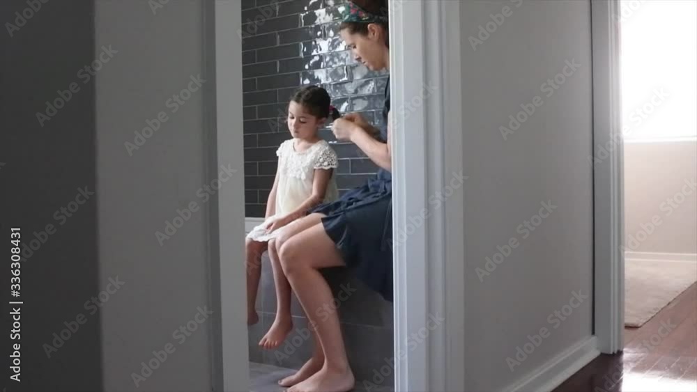 Mother braiding her daughters hair in bathroom. Domestic family life concept. Real people. Copy space Mother braiding her daughters hair in bathroom. Domestic family life concept. Real people. Copy space