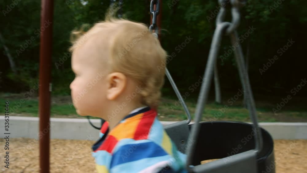 Close side view of little boy in toddler swing on summer afternoon Close side view of little boy in toddler swing on summer afternoon