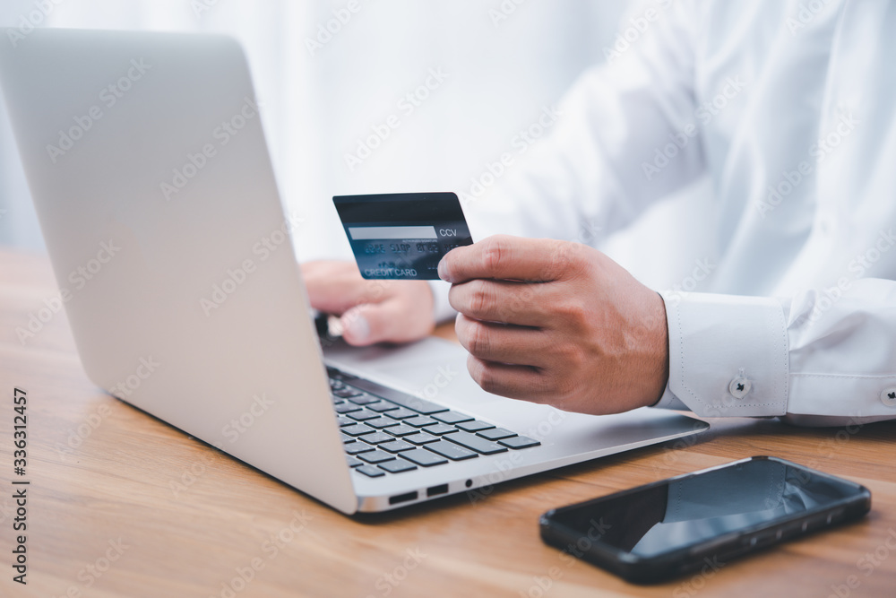 Hand holding credit card and using laptop. Businessman or entrepreneur working from home. Online shopping, e-commerce, internet banking, spending money, work from home concept. Hand holding credit card and using laptop. Businessman or entrepreneur working from home. Online shopping, e-commerce, internet banking, spending money, work from home concept.