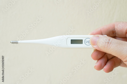 Hands holding a thermometer in order to measure fever for detecting COVIND19 symptoms illness.