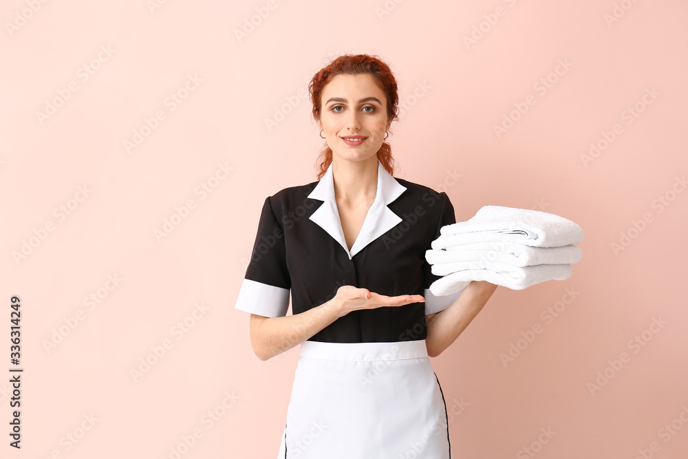 Fototapeta premium Beautiful young chambermaid with towels on color background