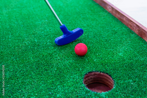 Mini golf. A golf club directs a red ball into the hole.