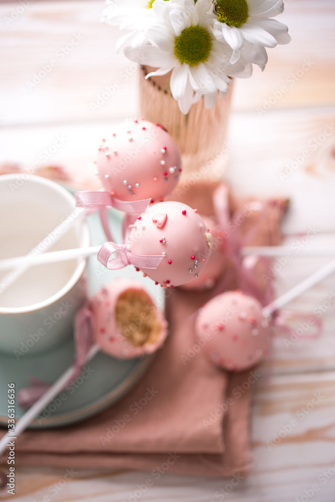 Cake pops in a light key in a beautiful utensil with pink chocolate cream and flowers on a wooden background. Cake pops in a light key in a beautiful utensil with pink chocolate cream and flowers on a wooden background.