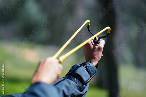 Slingshot aimed and pulled back against wrist, with hands - in forest setting photo