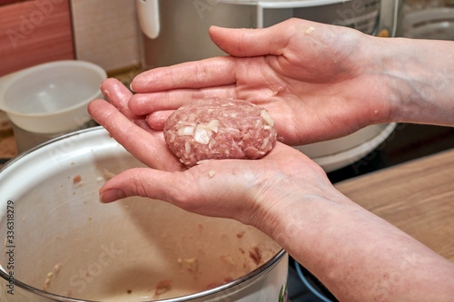 Woman hands sculpt a cutlet of minced meat in the kitchen. Homemade cutlets. Minced beef, pork and cabbage. In the background, a pot, a slow cooker, a Board and other dishes on the kitchen table.