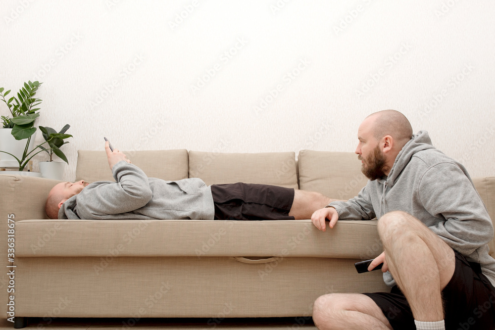 Fototapeta premium Collage of male cloned lies on a sofa and sits on the floor in various poses and uses a smartphone. Composite of multiple Human clones doing different activities at home during lockdown due to COVID 