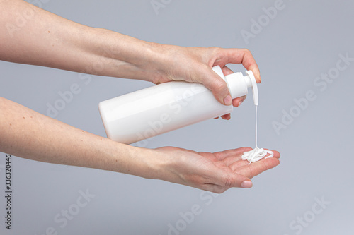 White people's hands using white body cream isolated in front of a grey background with structurant lights and shadows