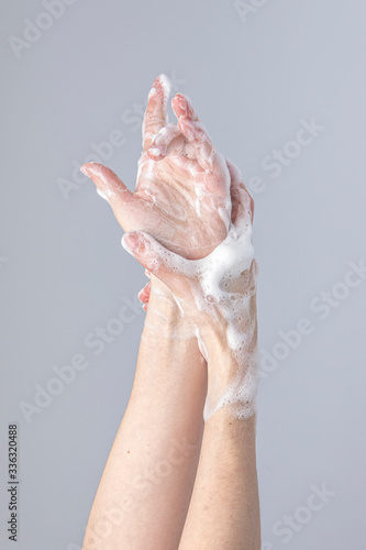 White people's hands washing each other with green foamy 
Marseille's soap isolated in front of a grey background with structurant lights and shadows