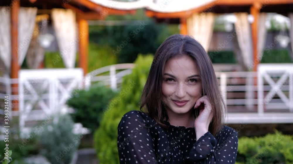 Close-up portrait of cute brunette girl in a black dress standing alone in park smiling looking at camera. Close-up portrait of cute brunette girl in a black dress standing alone in park smiling looking at camera.