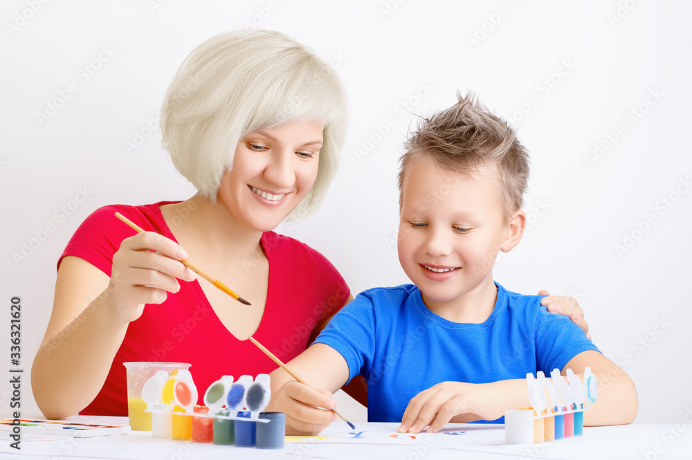 Fototapeta premium Happy smiling boy with messy hair and a cute girl with blond hair painting together on white paper. Leisure, education, family activities during quarantine concept