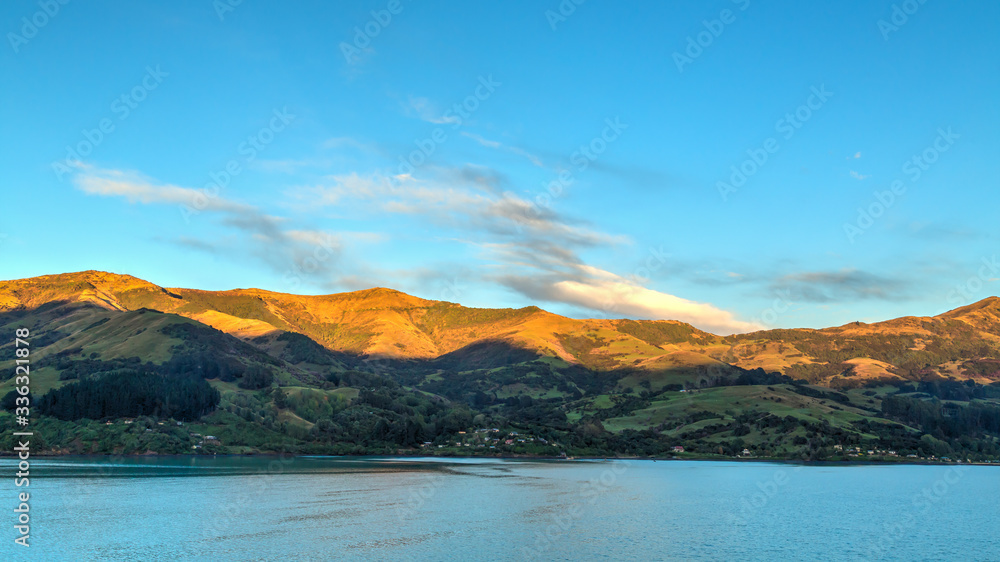 The rising sun lights up the tips of the mountains surrounding Akaroa Harbour on Banks Peninsula, New Zealand