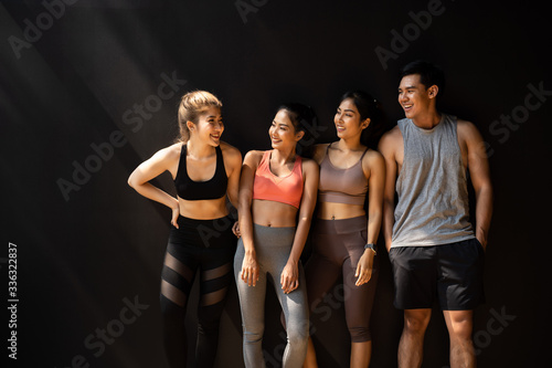 Happy smiling man and women having fun talking in gym. Group of young people relaxing in gym after workout training with black background.