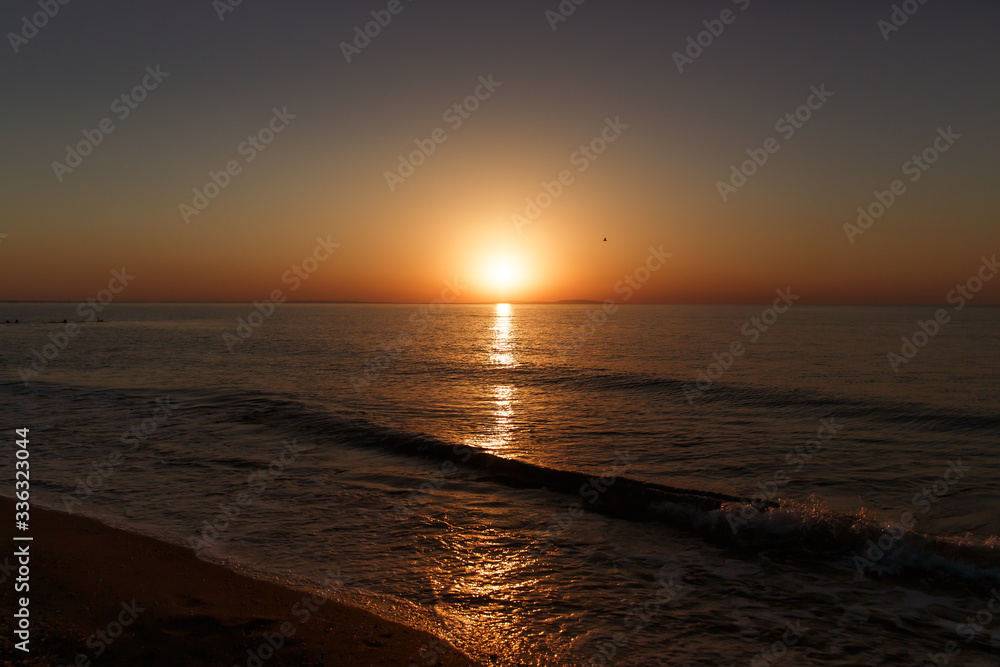 Obraz premium Sea coast at sunset, with the sun, wave, orange sky