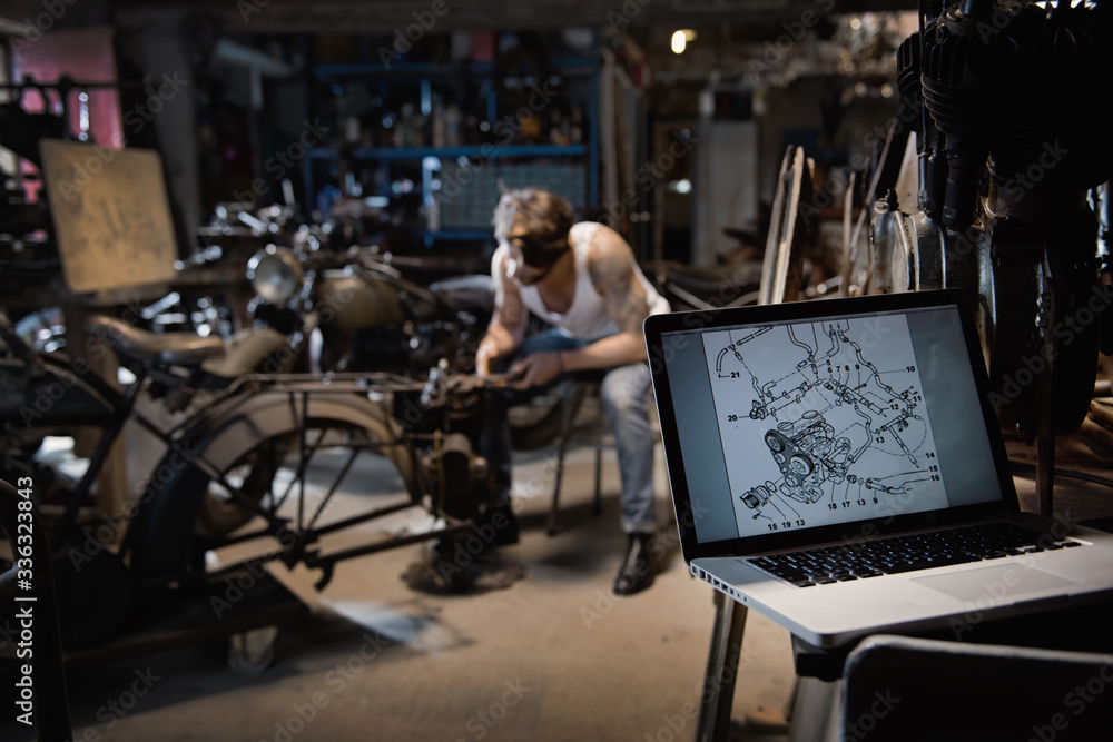Closeup on a laptop with a motor blueprint. A young man repairing vintage motorcycles