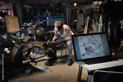 Closeup on a laptop with a motor blueprint. A young man repairing vintage motorcycles
