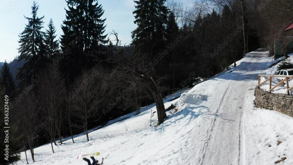 Man riding a snowboard and falling off after trying to do a frontflip, droneshot in snowy mountains and pine forest of krkonoce national park, czechia Man riding a snowboard and falling off after trying to do a frontflip, droneshot in snowy mountains and pine forest of krkonoce national park, czechia