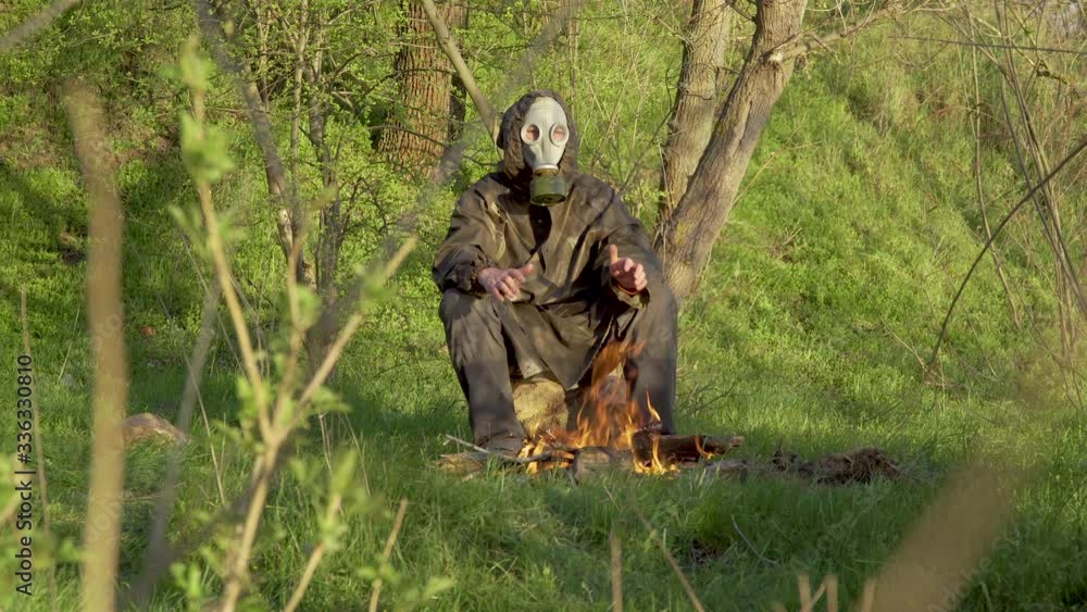 A man in a chemical protection suit and gas mask warms his hands over a fire. Personal safety concept for infectious epidemics, chemical or radioactive contamination. 4K A man in a chemical protection suit and gas mask warms his hands over a fire. Personal safety concept for infectious epidemics, chemical or radioactive contamination. 4K