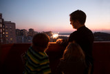 Family dad and two kids with Sparklers At sunset on the balcony of the home. Corona Virus. standing in home. chelter in place. end of a quarantine. home holiday
