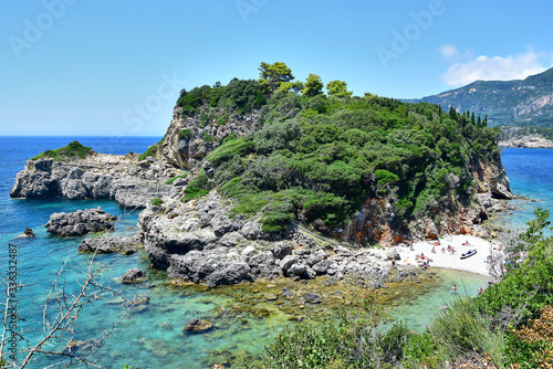 Paleokastritsa, Corfu Greece - Limni Beach, a cliff with green trees and bushes surrounded by turquoise water, a strip of beach covered with white pebbles is visible, blue sky in the summer afternoo. photo