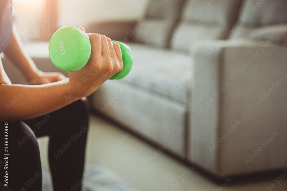 Close up woman lifting dumbbell weights for strength training while sitting at home.Sport and recreation concept. stay at home campaign for coronavirus prevention. Close up woman lifting dumbbell weights for strength training while sitting at home.Sport and recreation concept. stay at home campaign for coronavirus prevention.