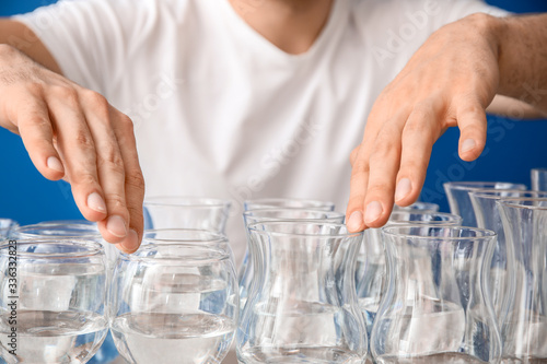 Young man playing music on glasses with water against color background, closeup