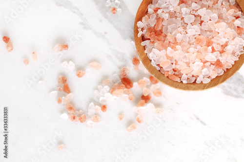 top view of himalayan pink rock salt in wooden bowl on white marble table with copy space.