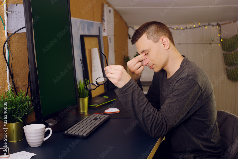 Fototapeta premium Stay at home, a man works at home. Freelance, a man studying a new program, online. A man with glasses sits at home at a computer; his eyes hurt. Computer vision problems