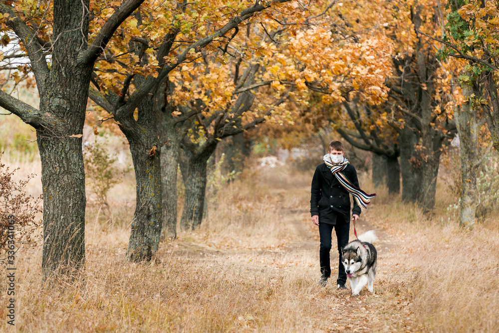 A man in a medical mask walks a dog in a forest during quarantine