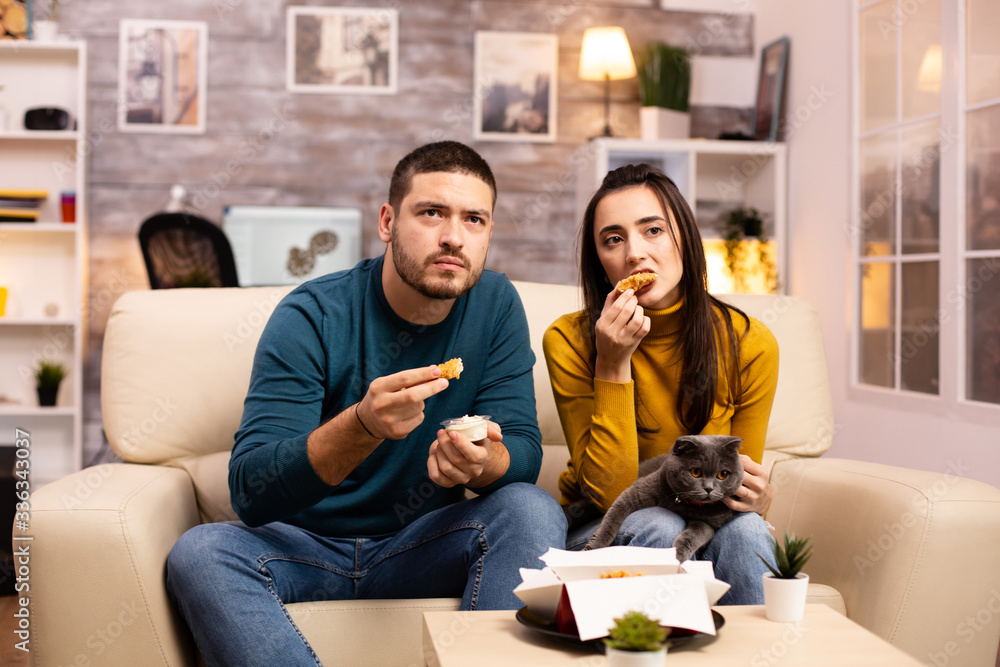 Young couple eating fried chicken in front of the TV Young couple eating fried chicken in front of the TV