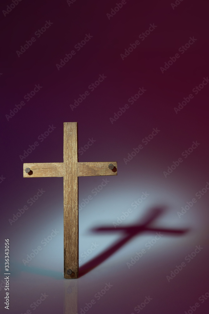 Wooden cross photographed using harsh light to make shadow cast onto the background. Shot in studio