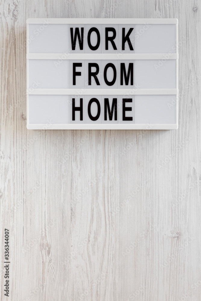 'Work from Home' words on a lightbox on a white wooden surface, top view. Overhead, from above, flat lay. Copy space.