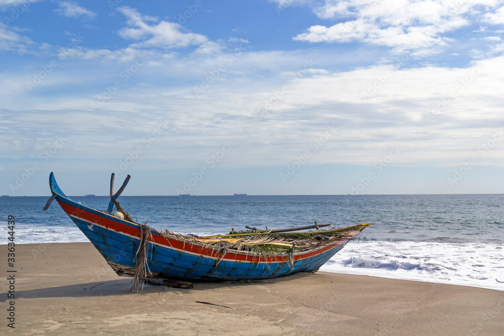 Wooden fishing boat on a deserted beach on a background of foam waves and a blue sky with clouds on a sunny day. Copy space