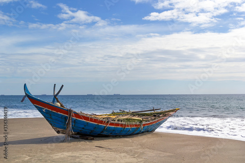 Wooden fishing boat on a deserted beach on a background of foam waves and a blue sky with clouds on a sunny day. Copy space © alexey_arz