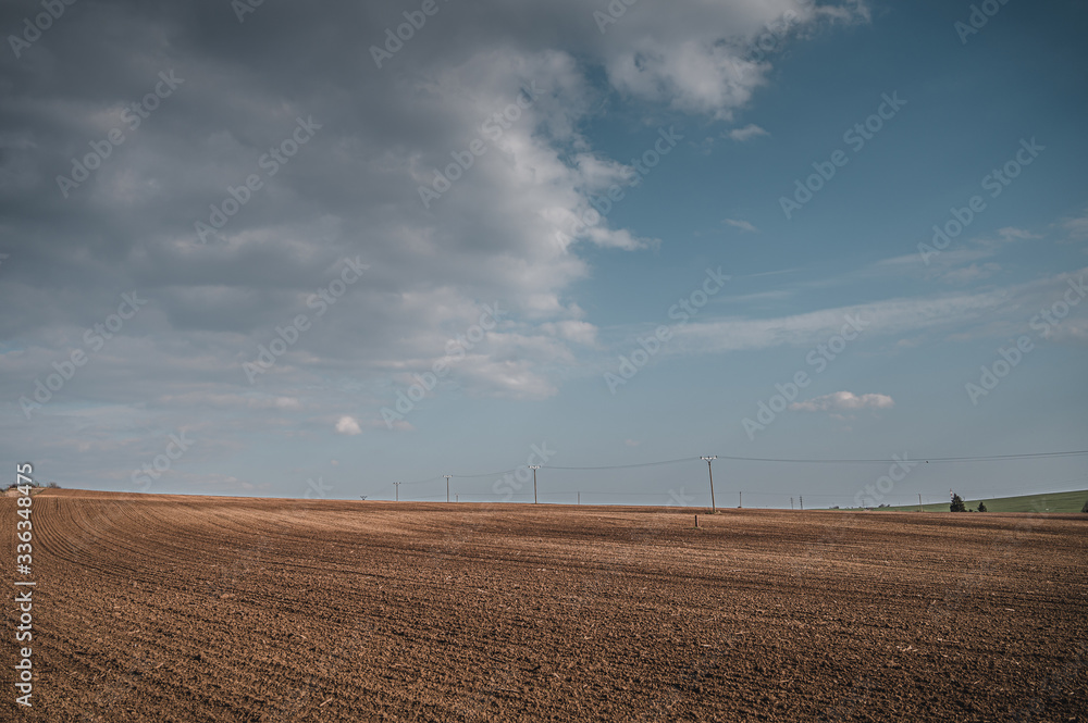 Spring field landscape. Blue sky with white clouds in background. Freshly plowed fields and electric poles.