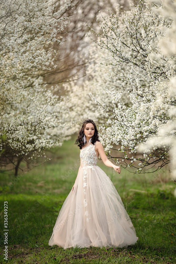 the bride in a wedding dress among the flowering trees holds a wedding bouquet, wedding day, beautiful portrait of a bride