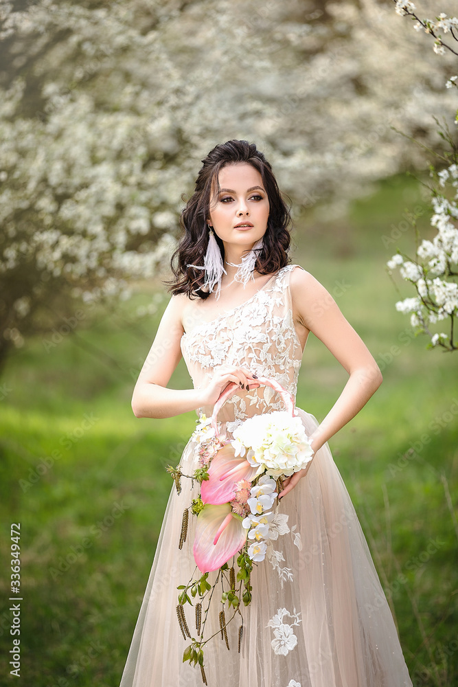 the bride in a wedding dress among the flowering trees holds a wedding bouquet, wedding day, beautiful portrait of a bride the bride in a wedding dress among the flowering trees holds a wedding bouquet, wedding day, beautiful portrait of a bride