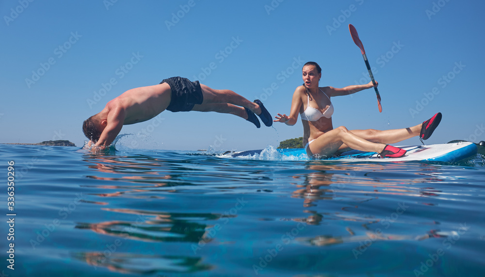 Young and beautiful couple of lovers sitting on a surfboard in the open ocean on a background of sky.