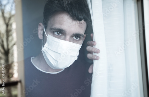Sick man of corona virus looking through the window and wearing mask protection. People recovery from coronavirus at home.