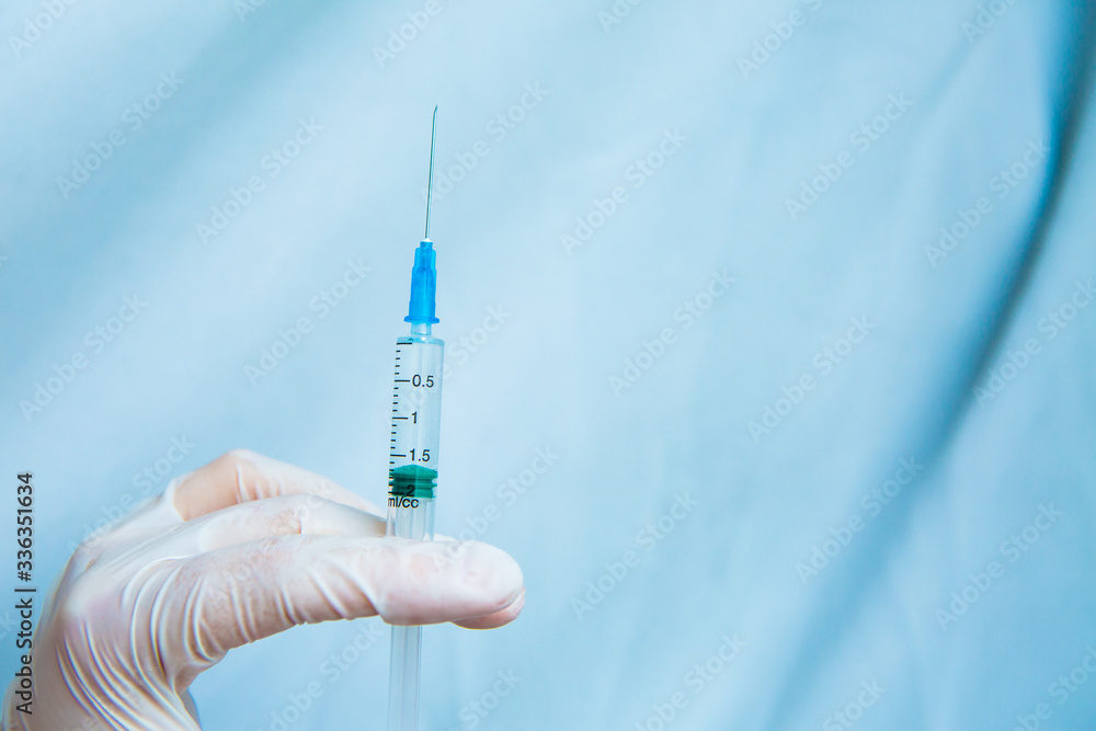 Hands in white gloves hold a syringe on a blue background. Coronavirus disinfectants, asian flu outbreak, Coronavirus 2019-nCoV, Corona virus outbreaking. Spray bottle Hands in white gloves hold a syringe on a blue background. Coronavirus disinfectants, asian flu outbreak, Coronavirus 2019-nCoV, Corona virus outbreaking. Spray bottle
