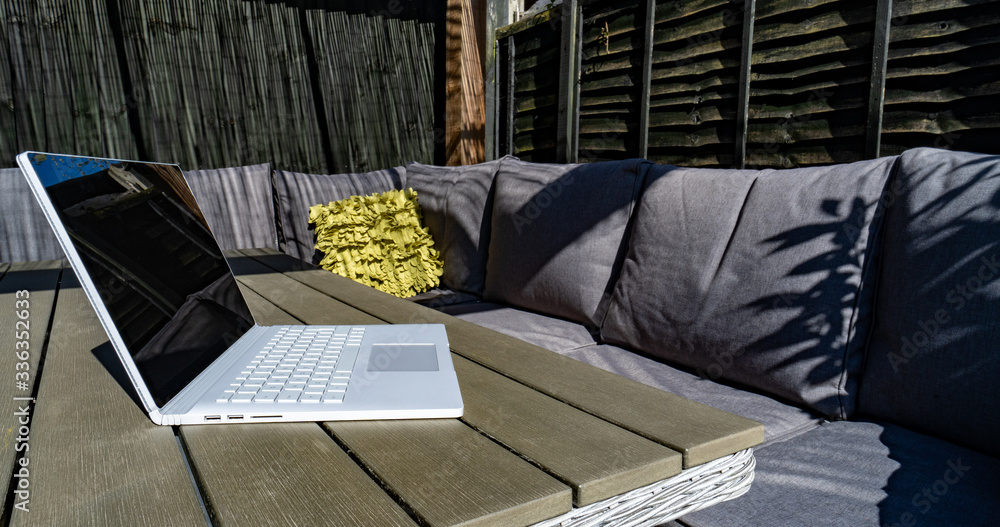 Summer working from home in the garden close up on debranded laptop and garden sofa set 