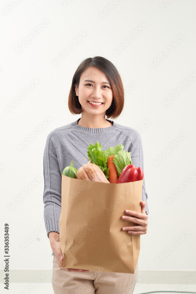 Beautiful smiling Asian woman holding paper shopping bag full of vegetables and groceries, studio shot isolated on white background Beautiful smiling Asian woman holding paper shopping bag full of vegetables and groceries, studio shot isolated on white background